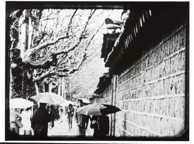 A film still showing people holding umbrellas on a snowy day next to a palace wall in Korea.