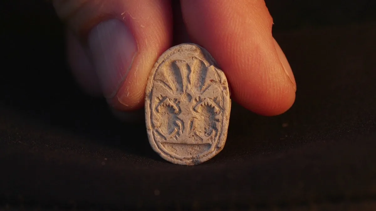 Two fingers holding an ancient amulet.