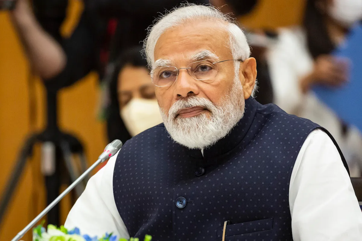 Portrait of Narendra Modi before a microphone.