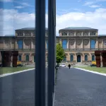 A museum building and a plaza reflected in a pane of glass.