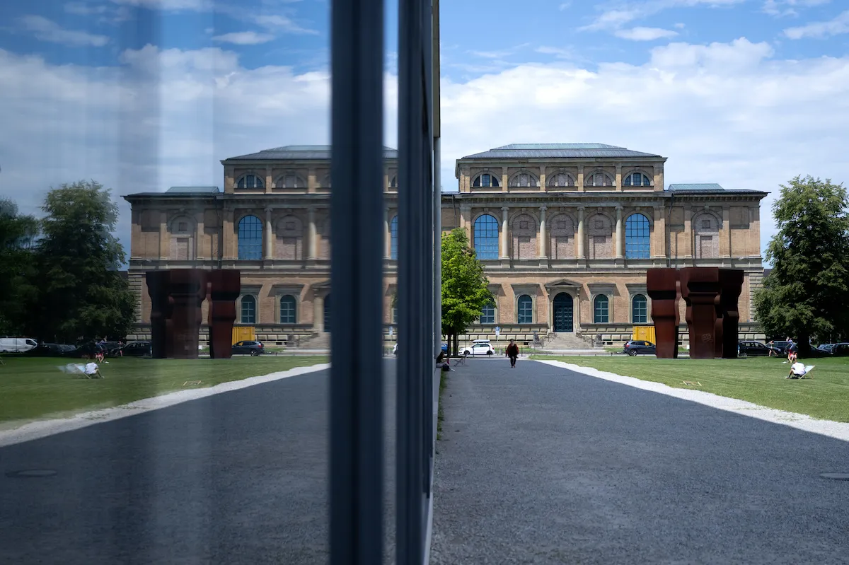 A museum building and a plaza reflected in a pane of glass.