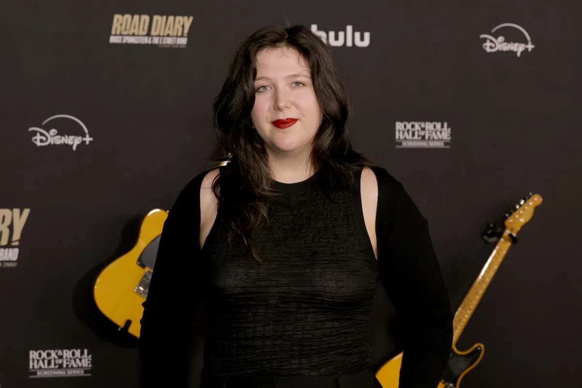 A woman standing on a red carpet before two guitars.