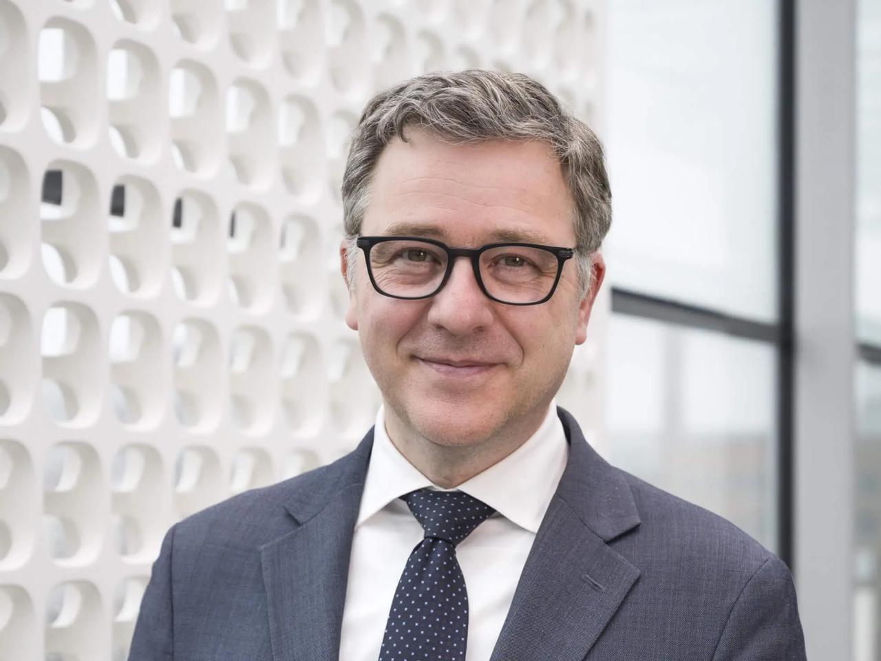 A man in a suit and glasses smiles at the camera.