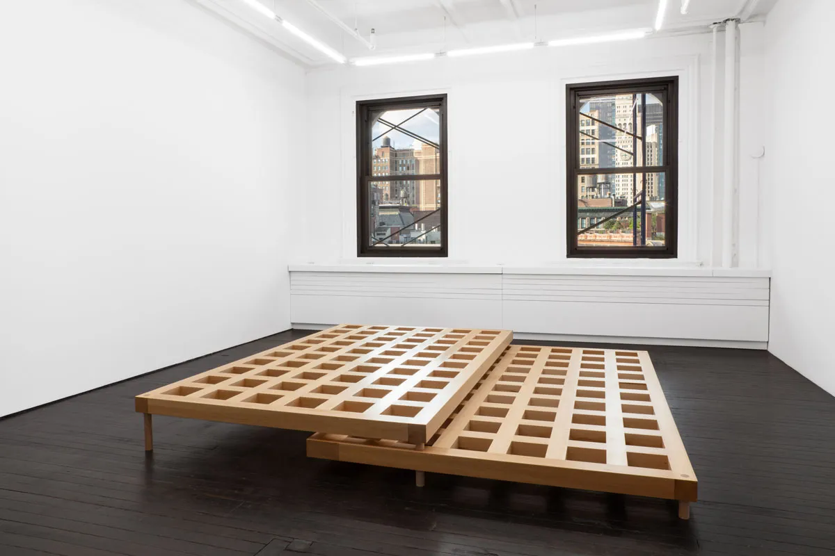 View of a small gallery showing a sculpture of two latticed wood elements that nestle on top of each other.