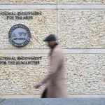 A person walking by a building with signs for the National Endowment for the Arts and the National Endowment for the Humanities.