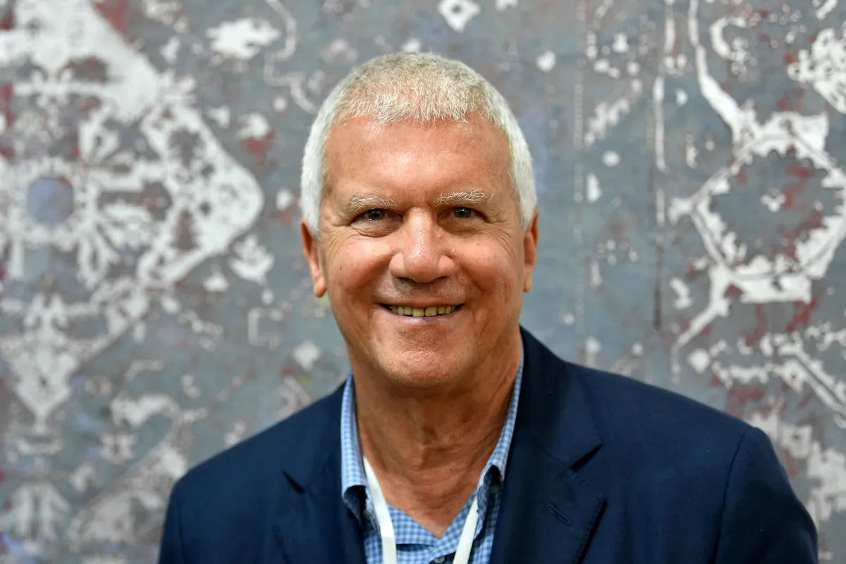 A smiling man wearing a suit in front of an abstract painting.