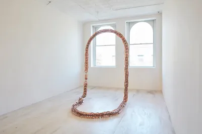 A necklace-like sculpture stood up in a gallery.
