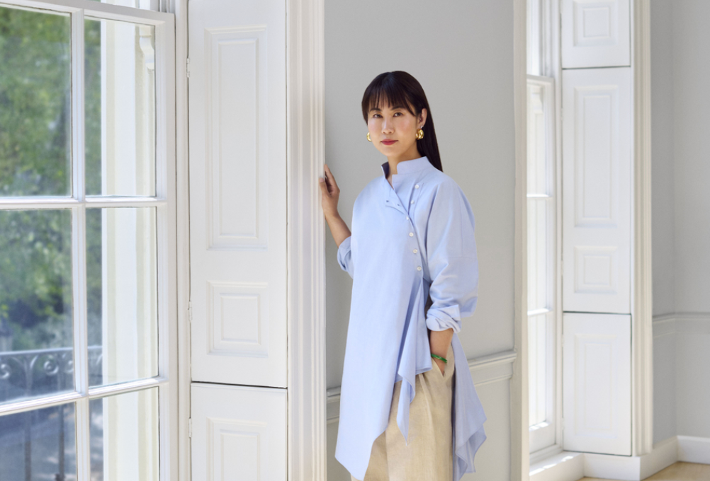 A Chinese woman stands next to a window.