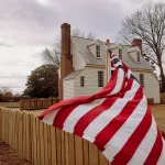 A US flag waves in front of a small school house.