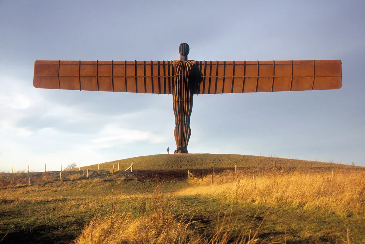 A monumental sculpture of an angel spreading its wings above a field.