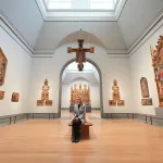 A person seated on a bench in a room filled with religious icons.
