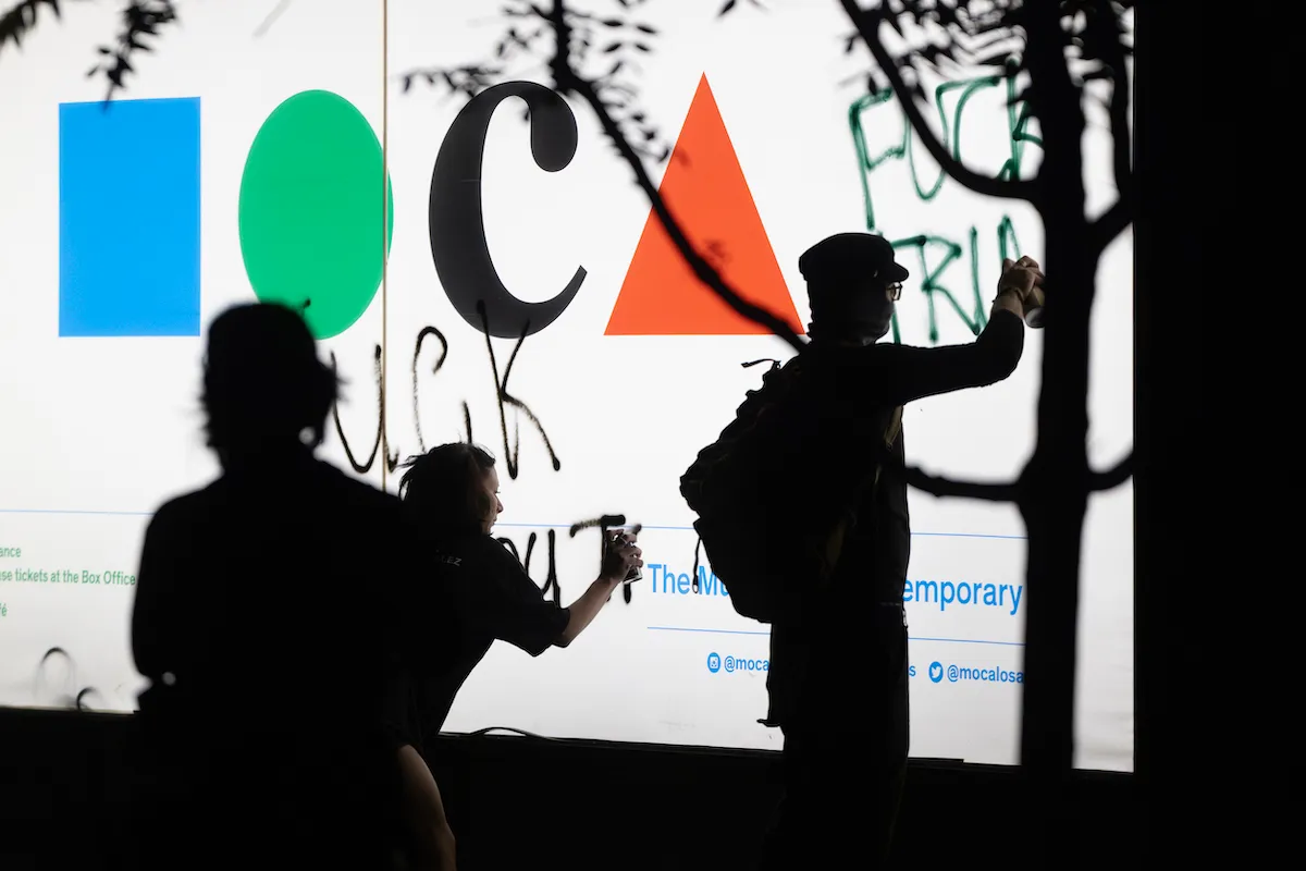 Protestors spray-painting phrases on a sign reading