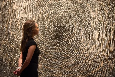 A woman standing in front of a work made from nails arranged in a spiral-like shape.