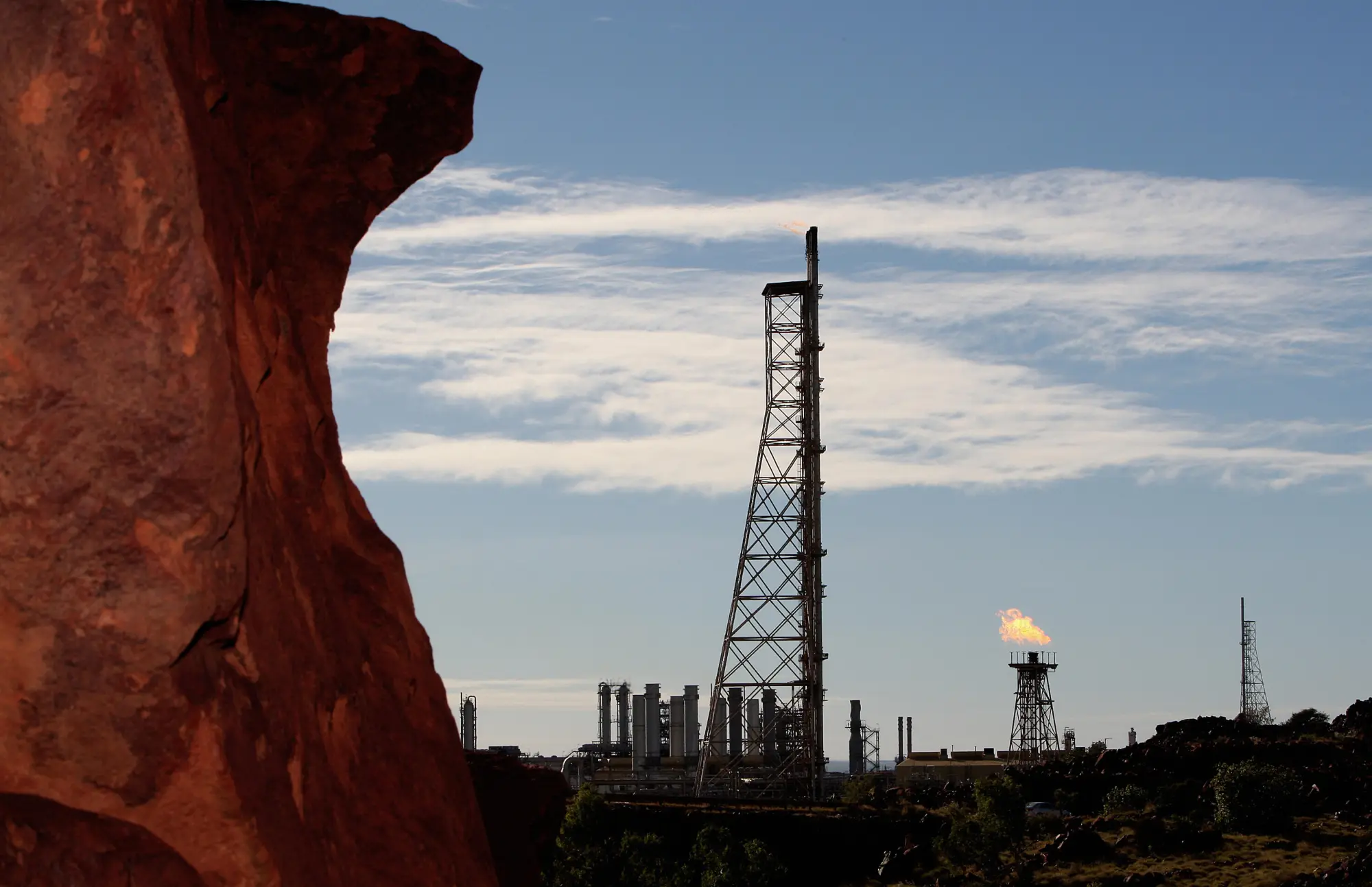 Gas flares (R-at back) at the Woodside operated North West Shelf Venture with rock (L-foreground) are shown on the Burrup Peninsula in the north of Western Australia on June 17, 2008. Piles of red rock which typify the Burrup area are the site for perhaps one million pieces of Aboriginal rock engravings several thousands of years old and considered by some to be the greatest concentration of such ancient art in the world. The peninsula in the resource-rich Pilbara region is also home to increasing amounts of industrial activity, including a gas processing plant, a fertiliser plant and iron ore facilities which are threatening the rock images of long-extinct animals and what are believed to be mythological creatures. AFP PHOTO / Greg WOOD (Photo credit should read GREG WOOD/AFP via Getty Images)