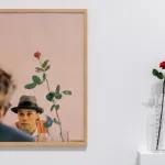 An actual rose in a vessel beside a photograph of a white man in a bowler hat beside a similar rose.