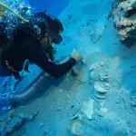 A diver carefully brushes sand away from stacked ceramics found in a shipwreck off the coast of Turkey.