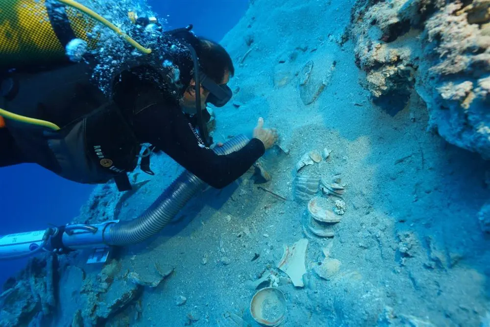 A diver carefully brushes sand away from stacked ceramics found in a shipwreck off the coast of Turkey.
