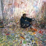 A painting of a man seated in a studio whose floor is covered in paint.