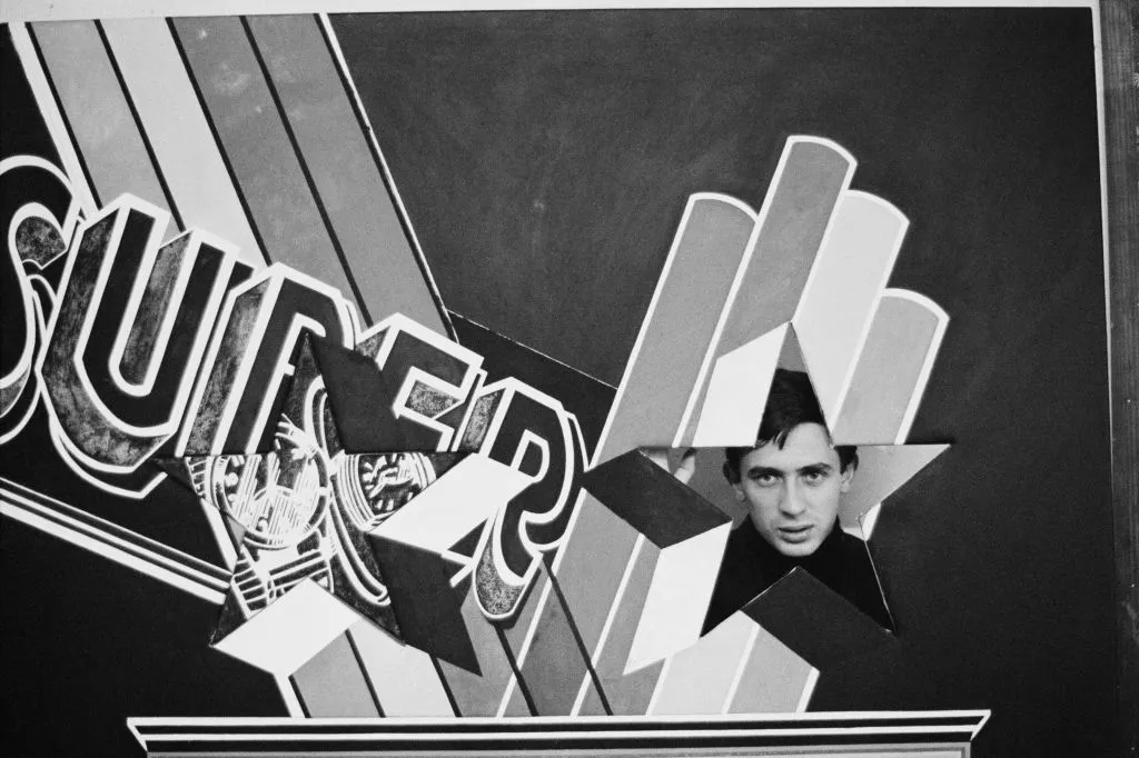 British pop artist Peter Phillips seen through a star-shaped hole in a version of his painting INsuperSET, ca. 1963.
