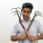 A man holding two rakes across his chest.