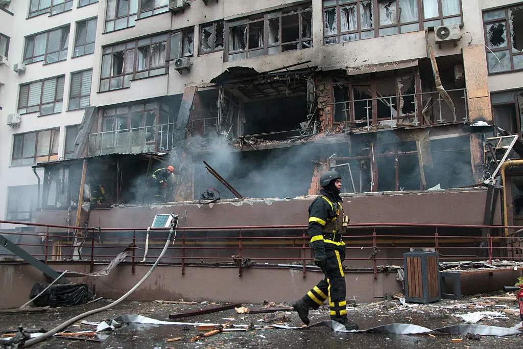 A burning building with smoke and a man in a black and yellow protective suit.