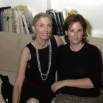 Two women seated together on a couch with books behind it.