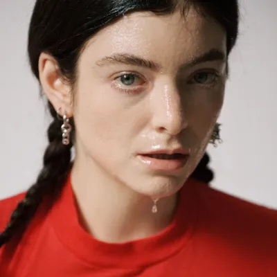 A woman with a long braid of hair in a red shirt. Her face is slicked with a semi-transparent substance.
