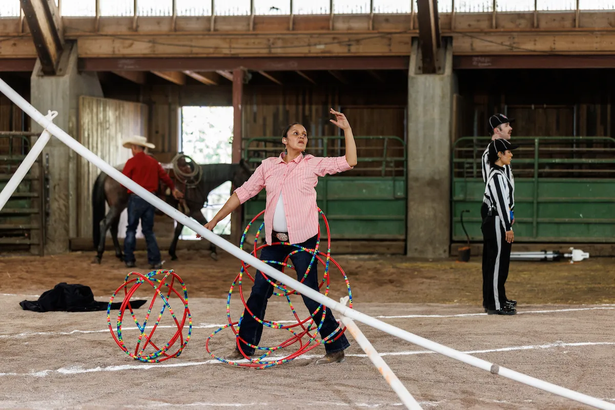 A hoop dancer surrounded by numerous multicolored hoops in front a horse and its handler, plus two football referees.