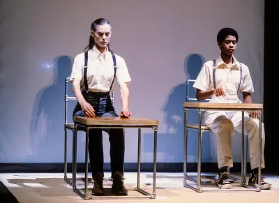 Two people rigidly seated at desks.