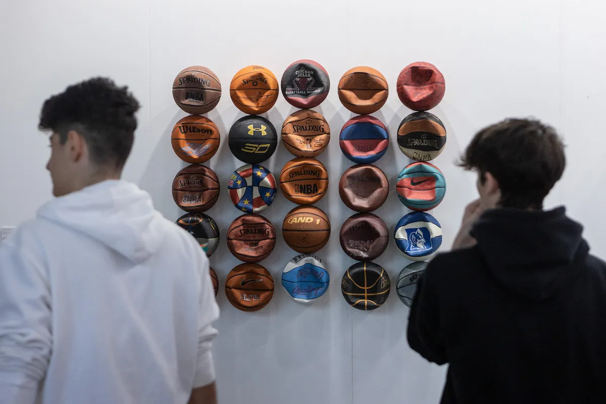 Two people standing in front of a sculpture featuring rows of deflated basketballs.