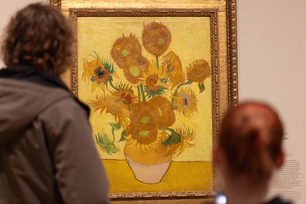 Two people staring at a painting of sunflowers in a vase.