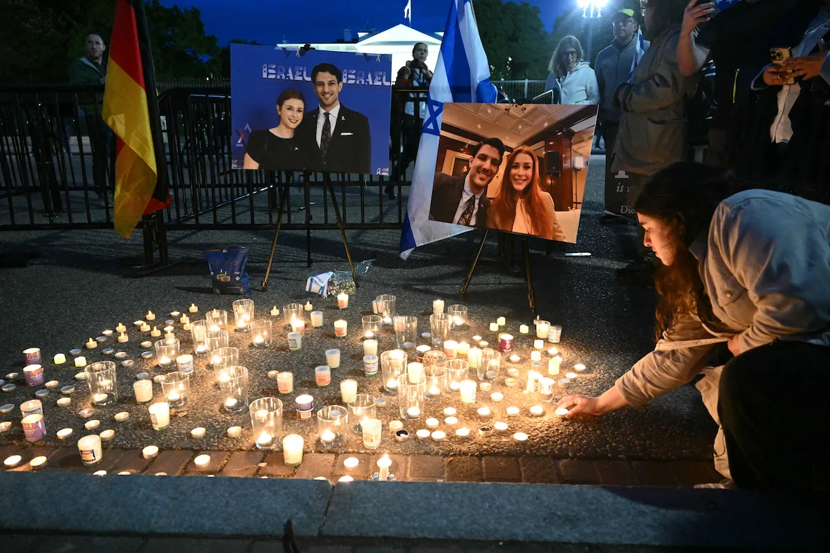 A person putting a lit candle on a ground strewn with other lit candles.