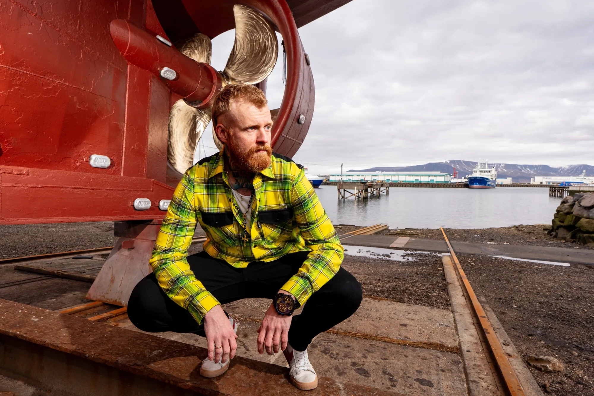 A man with red hair and a beard squats next to the propellor of a boat.