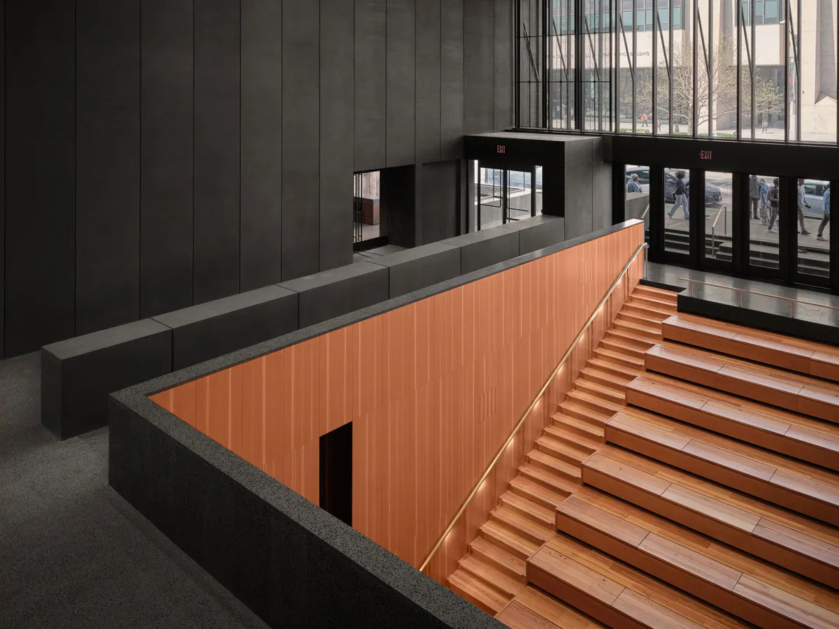 View of a wooden staircase and sitting area in a museum lobby that is nearly all-black.
