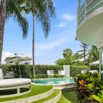 The facade of a home and a swimming pool surrounded by palm trees.
