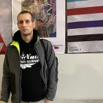 A man in a hoodie standing before three posters.