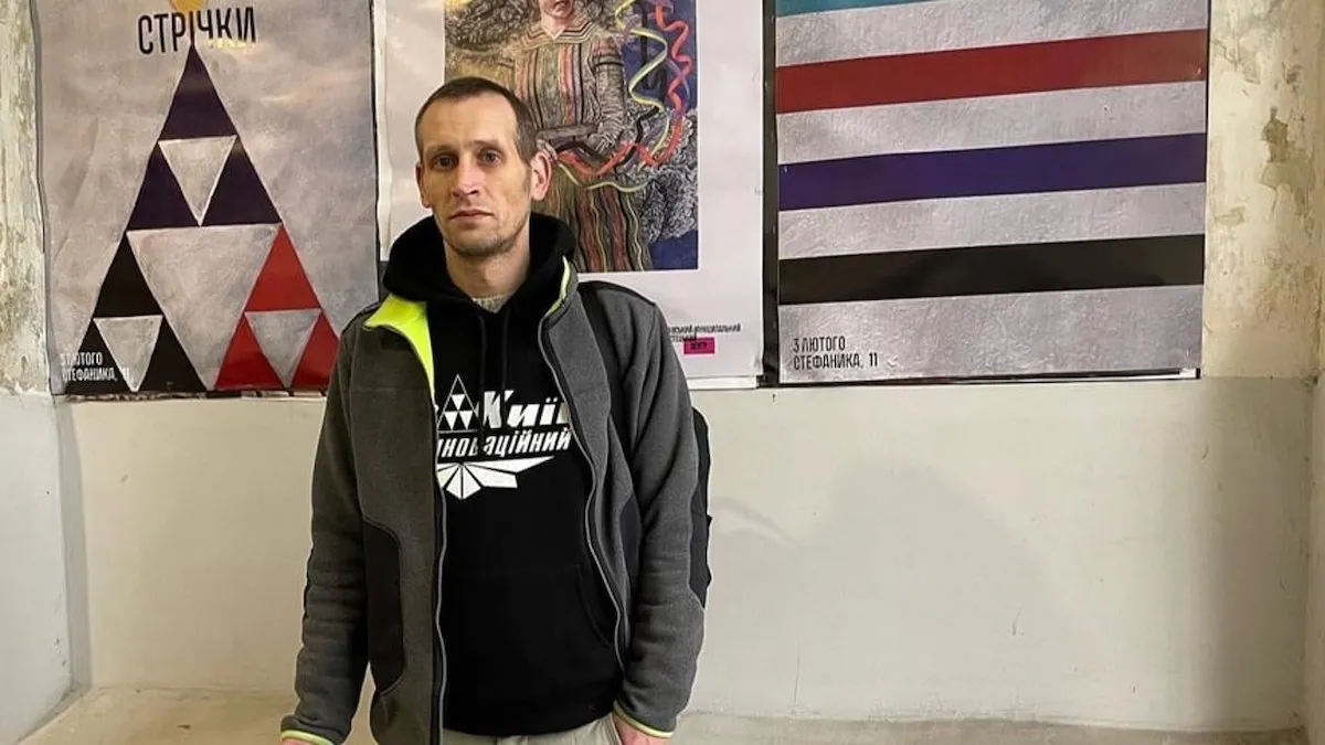 A man in a hoodie standing before three posters.