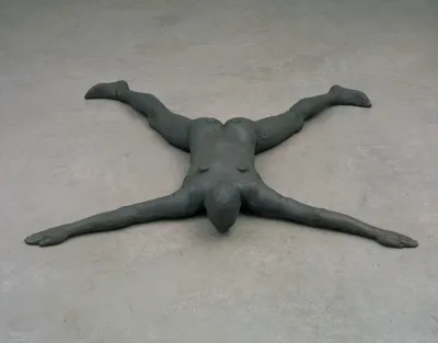 A sculpture of a figure splayed out and face down on the floor.