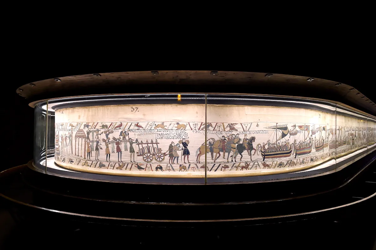 A long tapestry with various people, horses, and boats shown in a line.