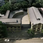 A building seen from an aerial view surrounded by trees in a city.