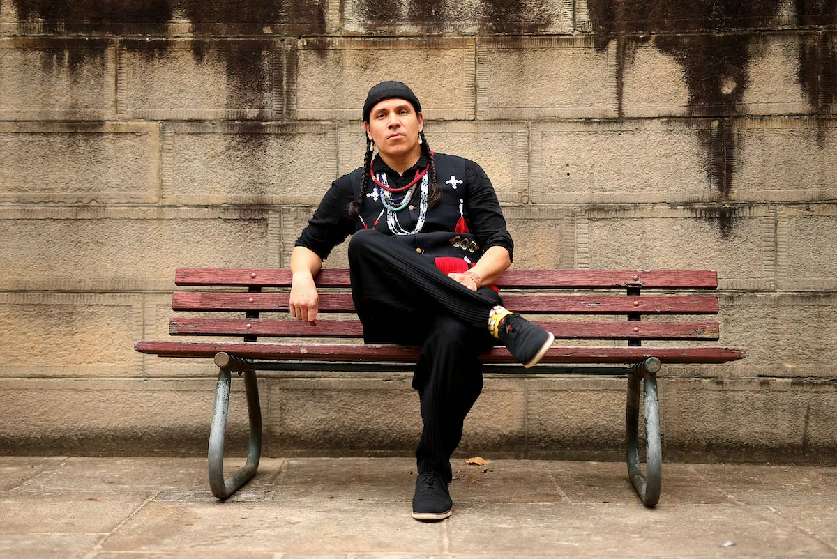 A man seated on a bench with one leg crossed over the other.