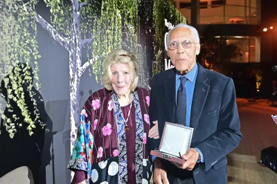 A woman in a dress beside a man in a suit holding an award.