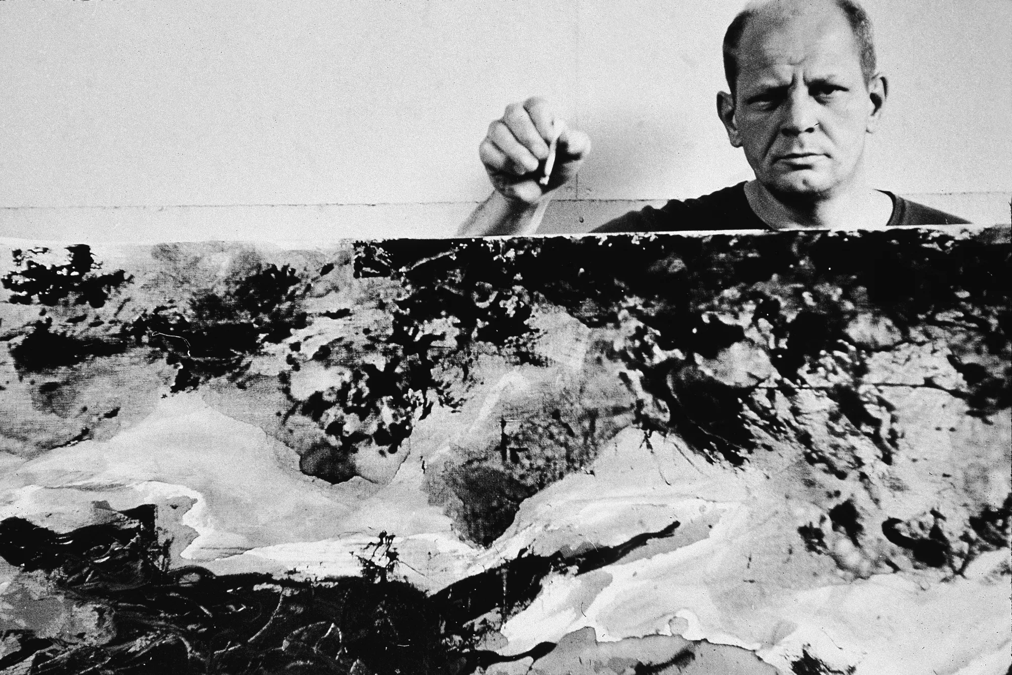 American abstract expressionist painter Jackson Pollock (1912 - 1956) holds a cigarette above as he stands behind a painting in his studio at 