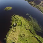 An aerial view of a green isle in the middle of a loch.