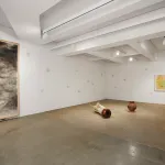 A gallery with a long paper work hanging on the wall and an installation featuring a large piece of wood.