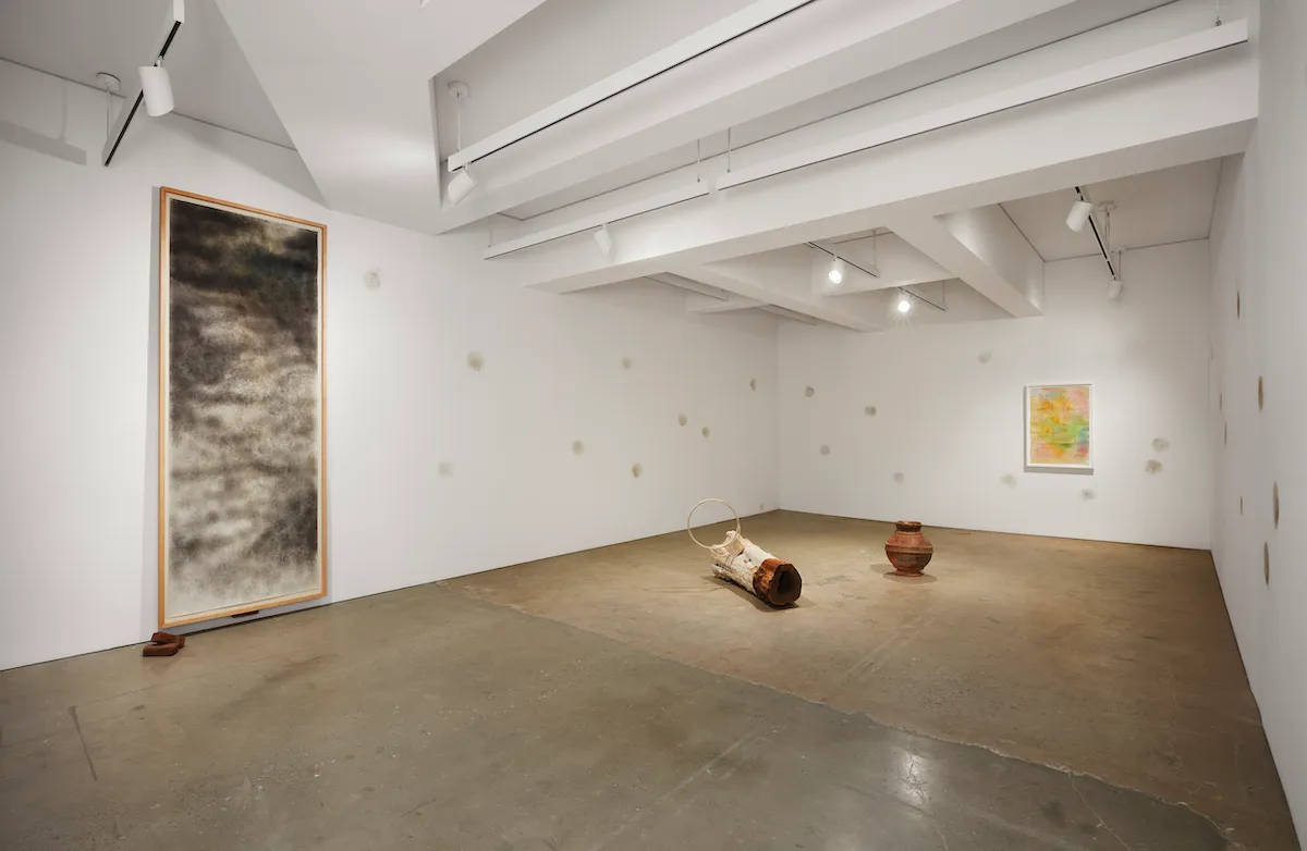 A gallery with a long paper work hanging on the wall and an installation featuring a large piece of wood.