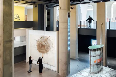 Two people pointing to an abstract painting. A person on a balcony above looks down at them.