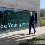 A man in a suit walks past glass windows.