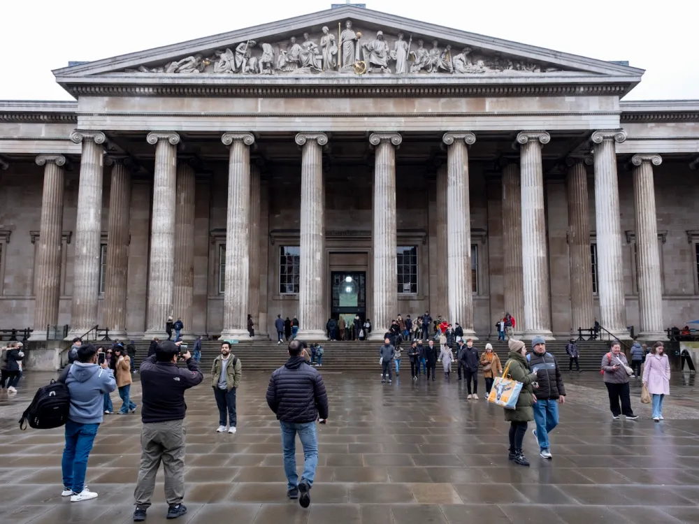 A classical looking structure with columns and people walking in front of it.
