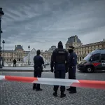 Three policeman standing before a glass pyramid.